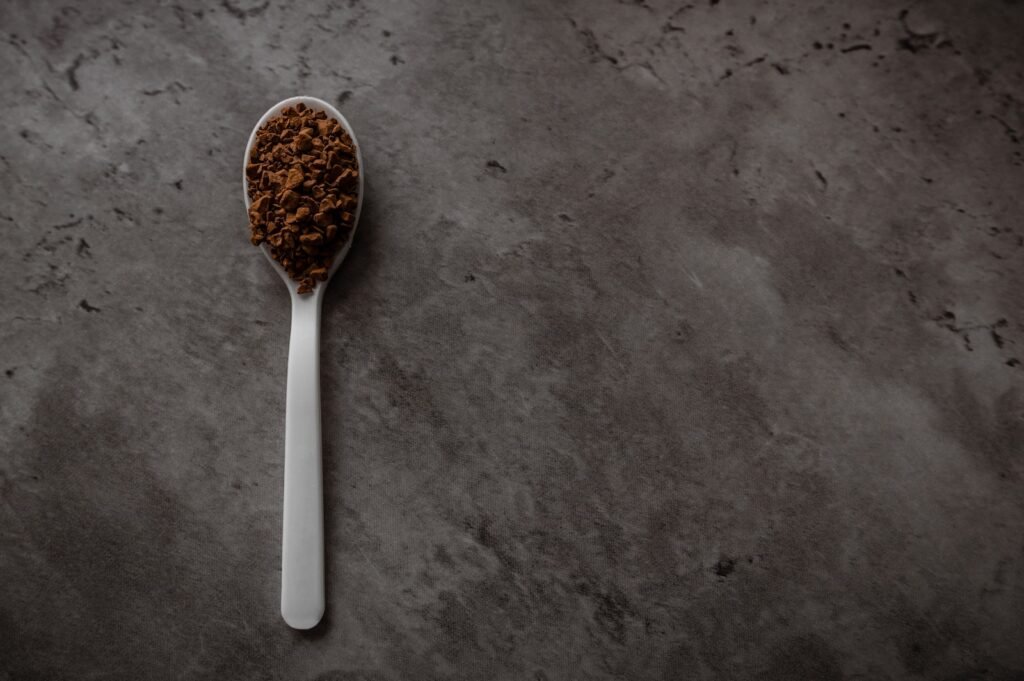 One spoonful of instant granulated coffee isolated on a dark kitchen counter. Top view flat lay with empty space for text on the right